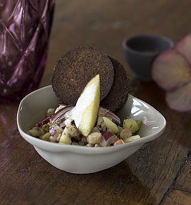 Matjestartar mit Kapern in kleinem Porzellanschälchen serviert mit zwei Pumpernickel